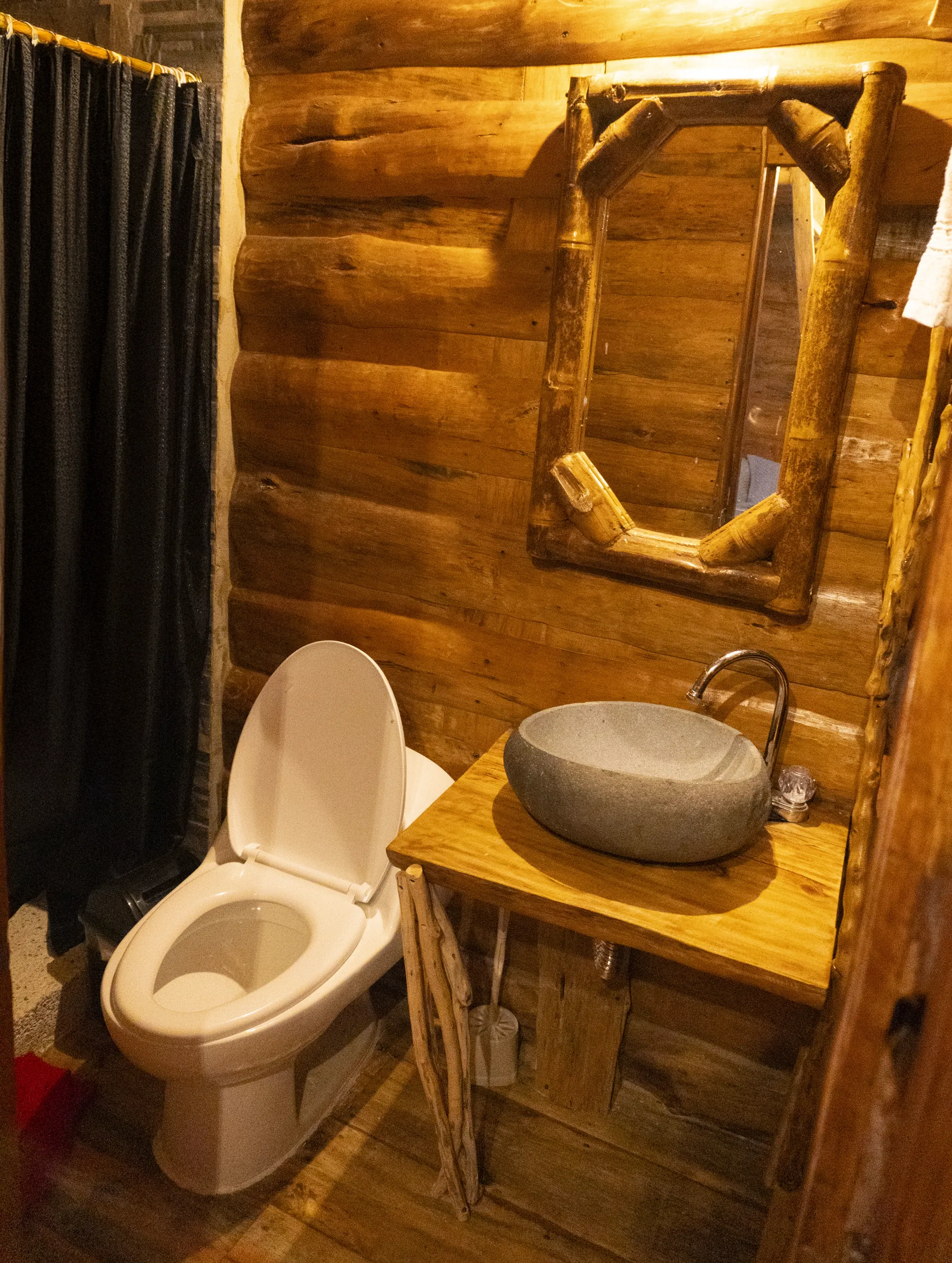 Baño de cabaña con lavamanos de piedra, espejo y sanitario