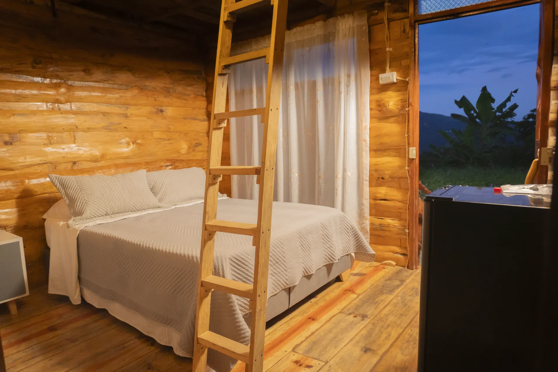 Cabaña Familiar Magdalena: habitación de madera con cama, escalera al altillo y televisor