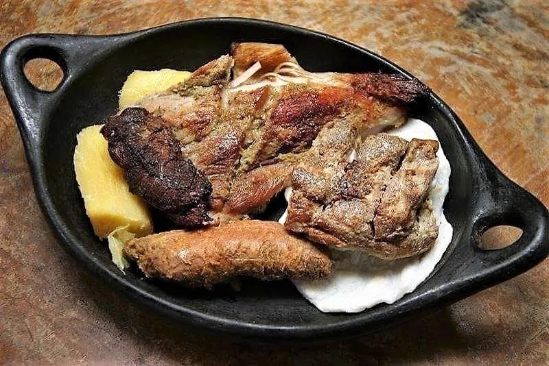 Picada campesina con carnes asadas, longaniza y yuca, servida en plato de barro negro